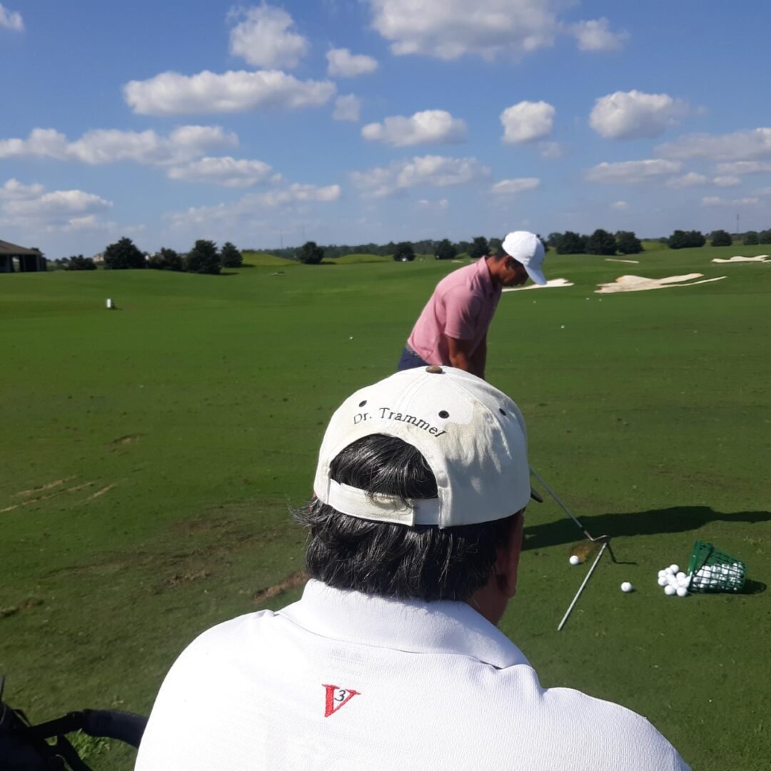 Dr. Richard Trammel observing a golfer during an on-course practice session, with his name visible on his cap