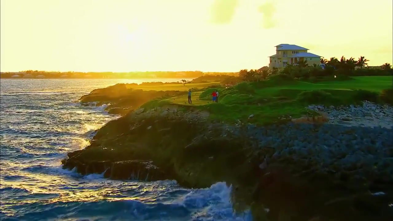 Waves rolling past a coastal golf course at sunset